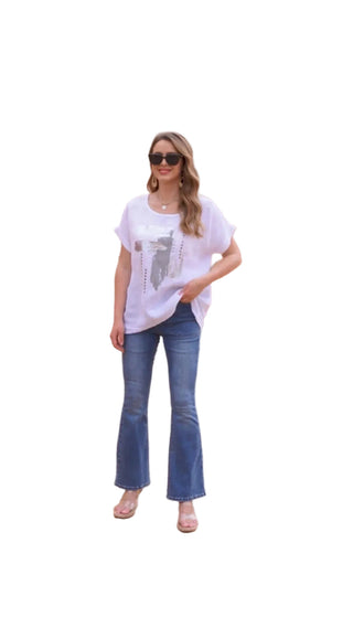 Woman in a white t-shirt and blue jeans standing in front of a pink architectural structure.