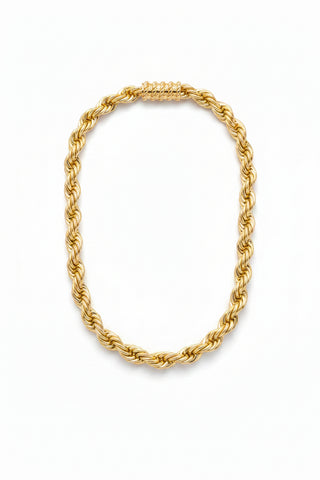 A chunky gold-toned rope chain necklace displayed on a black mannequin bust against a textured silver wall with circular cutouts.