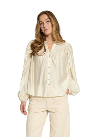 Woman wearing a cream blouse and pants against a white background