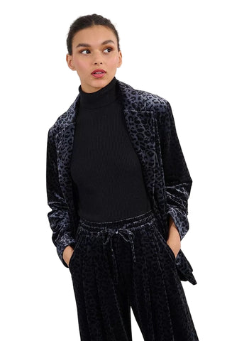 Person wearing a black leopard print blazer over a black turtleneck and black pants on a white background