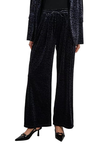 Black velvet pants with leopard print details worn by a person on a plain background